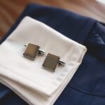 ネイビースーツと白いシャツの袖口に置かれた、オシャレなシルバーのスクエア型カフスボタン