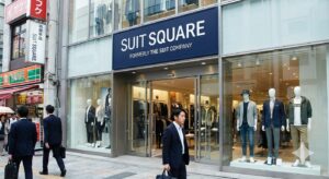 SUIT SQUARE(スーツスクエア)の店舗外観。「FORMERLY THE SUIT COMPANY」という看板があり、旧ザ・スーツカンパニーからのリブランディング店舗であることが分かる。最新のビジネスカジュアルやスーツが並ぶウィンドウディスプレイ。